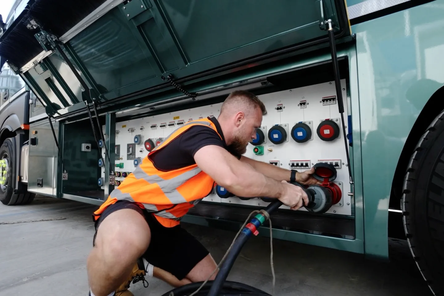 A worker in high vis connects a power cable to a stage V generator truck